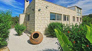 A modern stone building with a flat roof, large windows, and a gravel pathway leading to the entrance. - Villa Georgios Rafaela (Goudi)