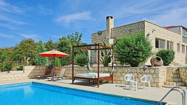 A swimming pool with a wooden canopy and lounge chairs, surrounded by stone walls and greenery. - Villa Georgios Rafaela (Goudi)
