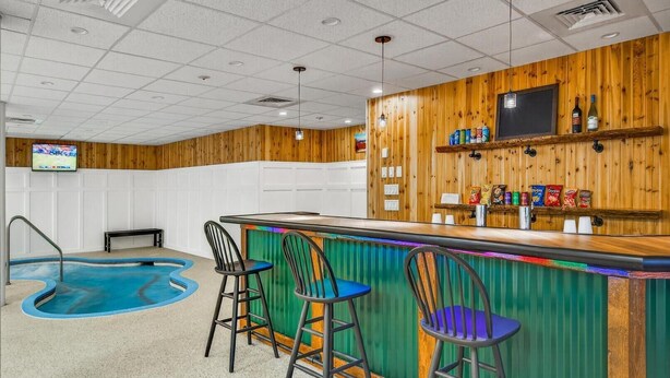 A pool area with a bar and stools, a television mounted on the wall, and wooden paneling. - Pinnacle A05 (Killington)