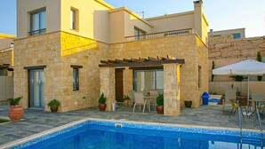 Une maison moderne à deux étages, dotée d’une façade en pierre, d’une piscine et d’un espace de détente extérieur.