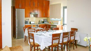 Un coin repas avec des chaises en bois et une table dressée pour six personnes, une cuisine avec des meubles en bois et des appareils électroménagers, et un radiateur dans un coin.