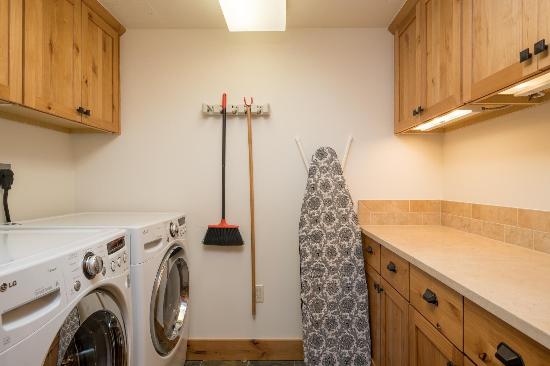 Une buanderie équipée d’un lave-linge et d’un sèche-linge à chargement frontal, d’un balai et d’une planche à repasser.