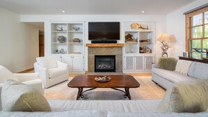 Uma sala de estar com lareira, móveis brancos e prateleiras decorativas.