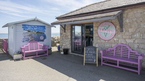 Una heladería frente al mar, con paredes de piedra, dos bancos rosas y un letrero que anuncia helados artesanales.