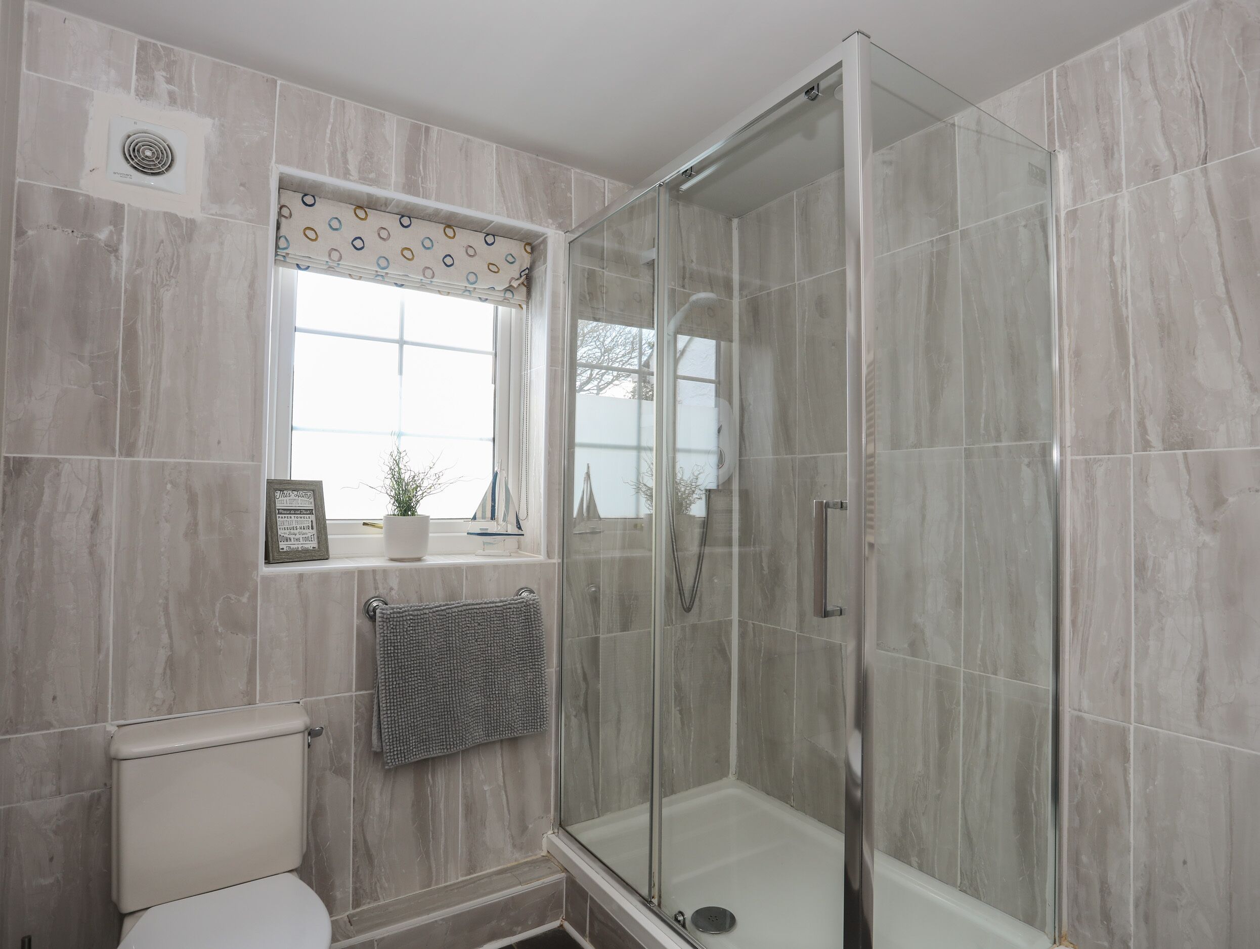A modern bathroom with a glass-enclosed shower, a toilet, and a window with a patterned curtain.