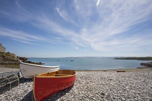 A pebbled beach with two boats, one white and one red, and a rocky shoreline. - Ty'n Lon (Dulas)