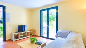 A living room with a sofa, a coffee table with a plant, a TV on a stand, and a sliding glass door leading to a garden. - Tinas Apartment in Mparmpati (Corfu)