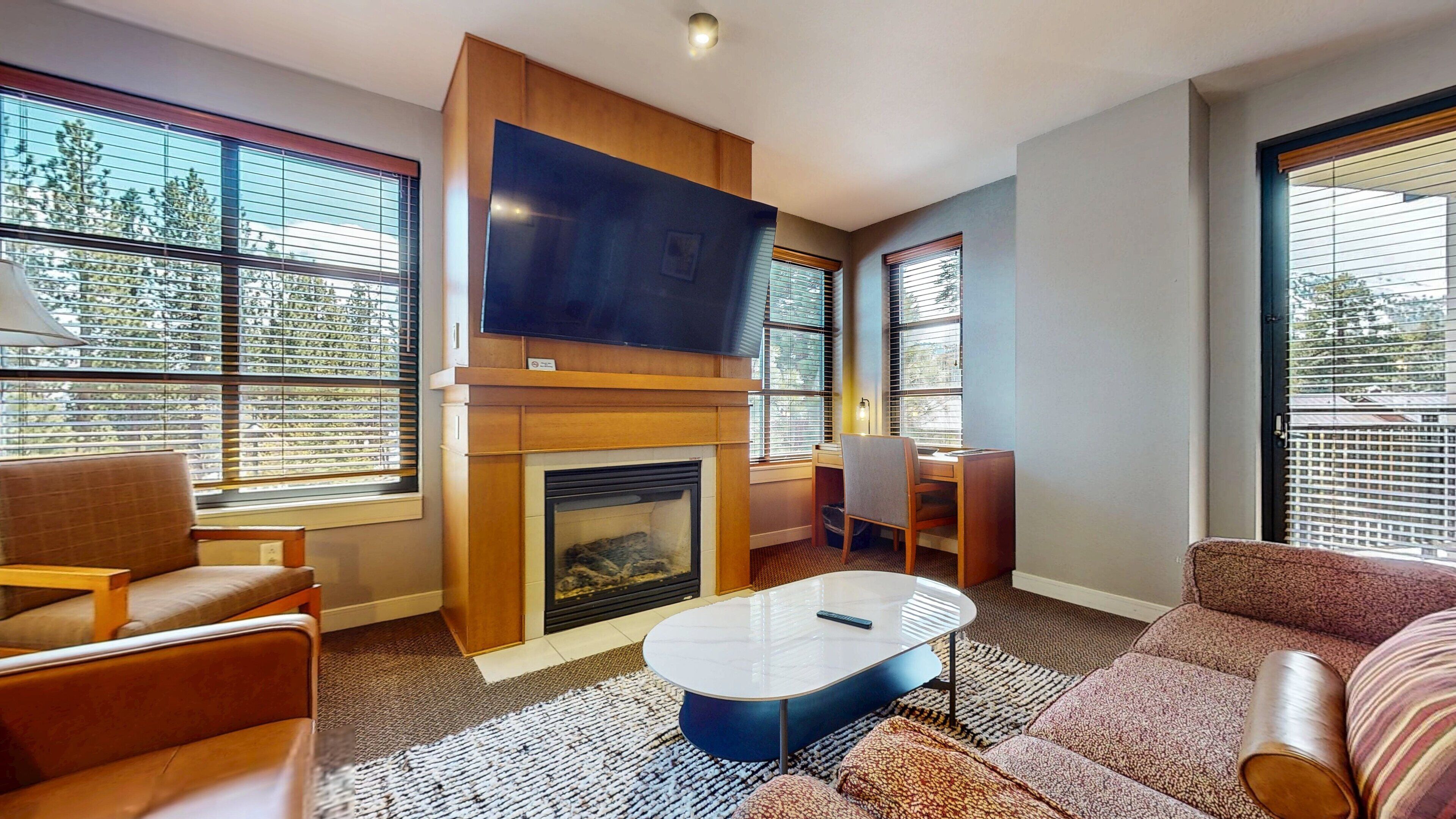 A modern living room with a fireplace, a flat-screen TV, and large windows.