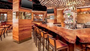 A bar area with wooden paneling, bar stools, and a variety of bottles and glasses on shelves. - Village Monache #311 2 Bedroom Condo by RedAwning (Mammoth Lakes)