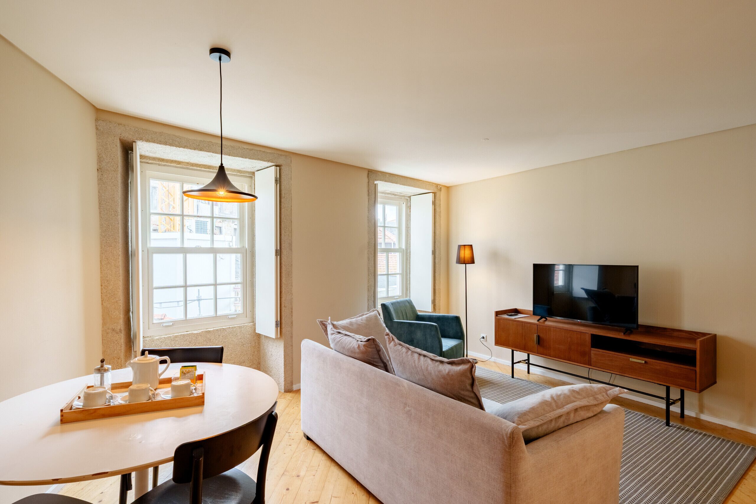 A living room with a sofa, a TV, a table with a tray of cups, and a hanging light fixture.