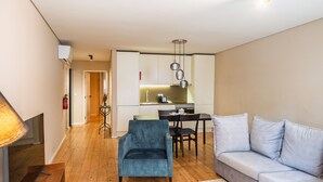 A modern living room with a sofa, a blue armchair, a dining table with chairs, a kitchen area, and a TV. - Quite One-Bedroom Apart for 3 in Center (Oporto)
