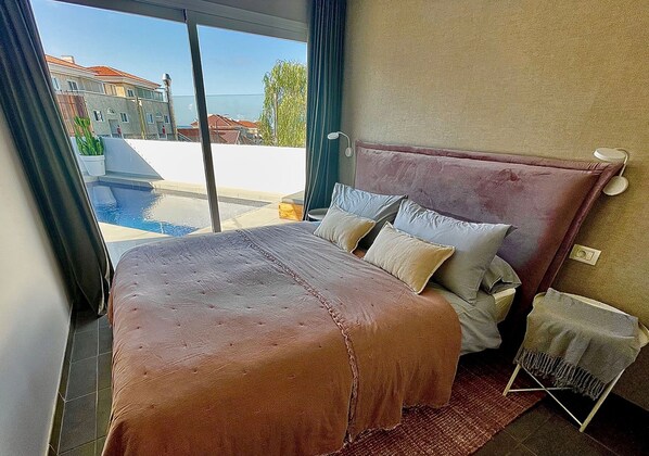 A bedroom with a large bed, a view of a swimming pool, and a balcony.