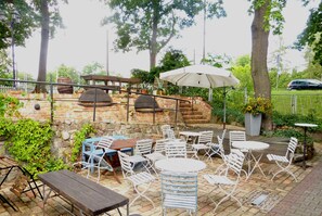 An outdoor patio with brick flooring, metal and wooden tables, and chairs.