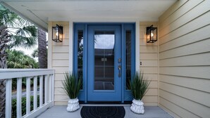 A blue front door with a glass panel, white potted plants, and two wall-mounted lanterns on a porch with a white railing. - Home on Beach Boardwalk! Private Pool! Amenity Cards! (Seabrook Island)