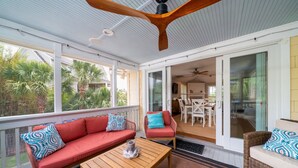A covered outdoor area with a wooden table, red and blue patterned sofas, and a ceiling fan. - Home on Beach Boardwalk! Private Pool! Amenity Cards! (Seabrook Island)
