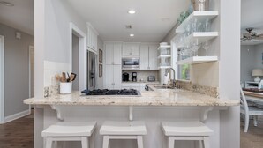 A modern kitchen with white cabinetry, a granite countertop, and a built-in island with bar stools. - Home on Beach Boardwalk! Private Pool! Amenity Cards! (Seabrook Island)
