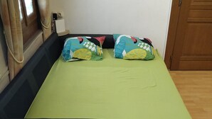Een eenpersoonsbed met een groene matras, twee kleurrijke kussens, een zwart hoofdbord en een houten vloer.