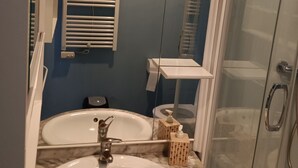 Een badkamer met een witte wastafel, een spiegel, een handdoekrek en een glazen douchecabine.
