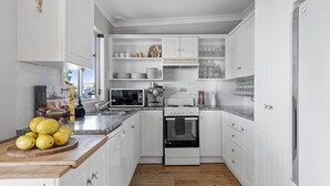 A kitchen with white cabinets, a microwave, stove, and a sink. There are lemons on the counter and a book titled "The Food of the World".