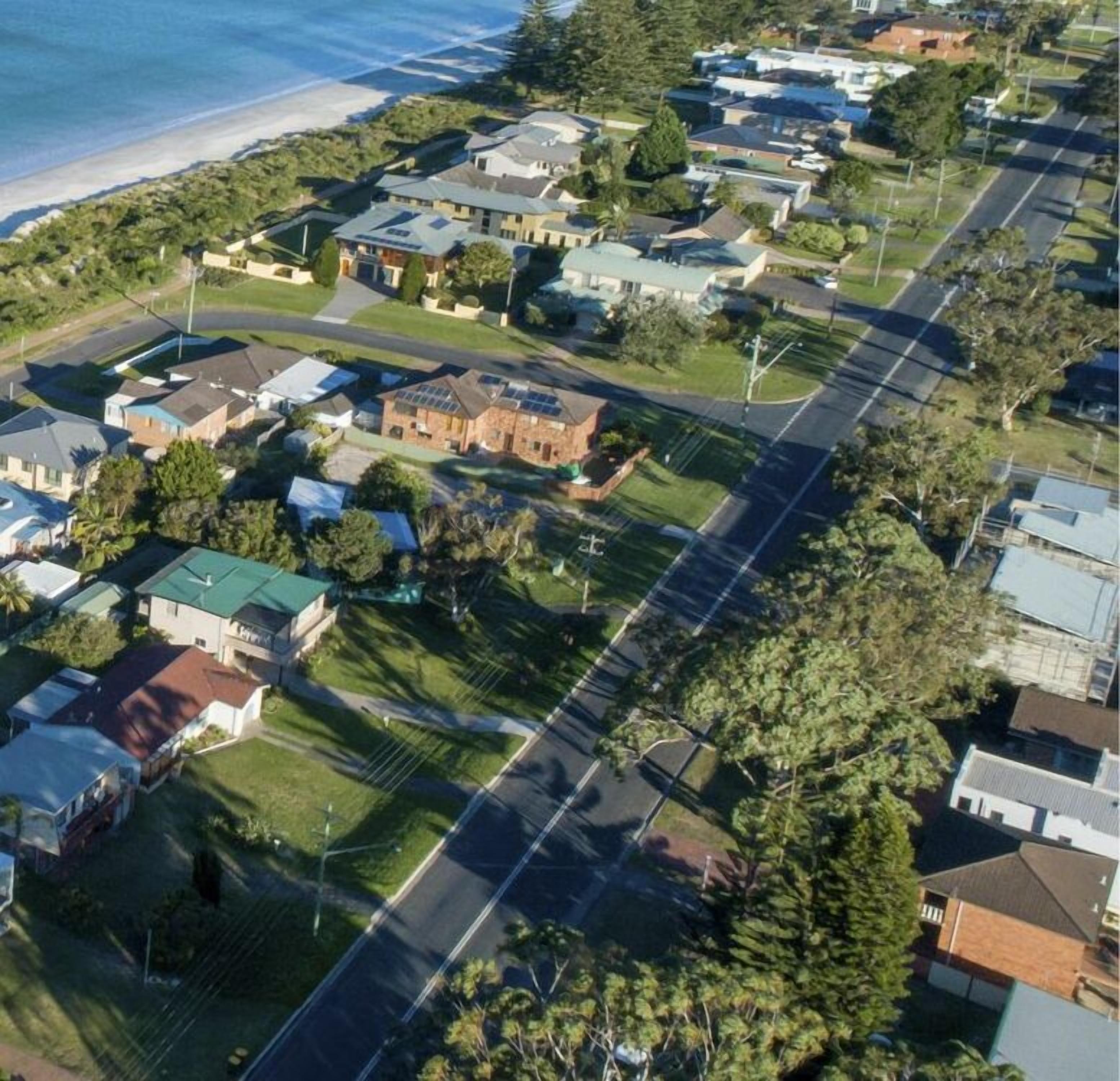 An aerial view of a residential area with houses, a main road, and a beach in the background.