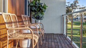 A balcony with wicker chairs and a white bucket, wooden deck, and a view of a green landscape.