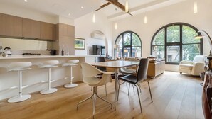 A modern kitchen with white bar stools, a dining table, and chairs. There are large windows with arched tops and a chandelier. - "The Sophia" Milan meets New York in Melbourne (Cremorne)