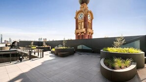 A rooftop terrace with modern outdoor seating, a large clock tower, and a city skyline in the background. - "The Sophia" Milan meets New York in Melbourne (Cremorne)
