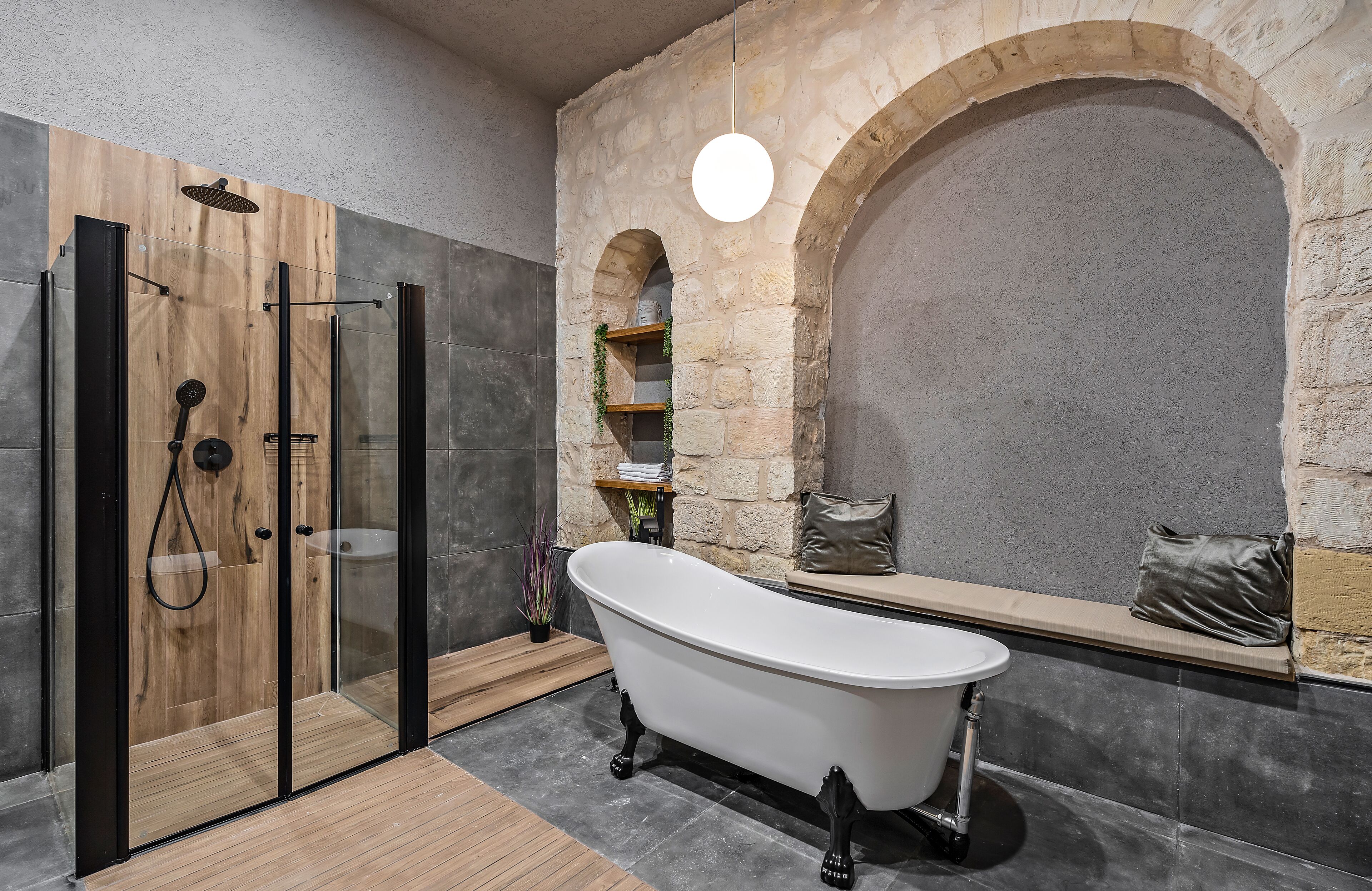 A bathroom with a freestanding bathtub, a glass-enclosed shower, and stone walls.