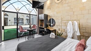 A modern hotel room with a large bed, a desk, a chair, a TV, and a view of the outside.