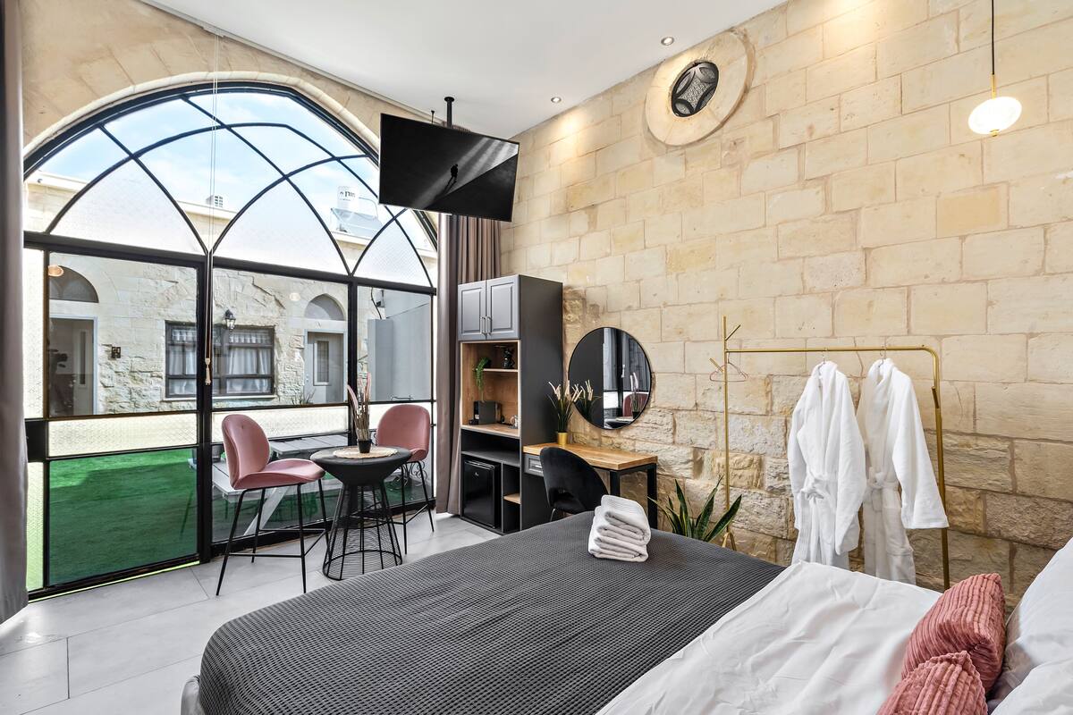 Ein modernes Hotelzimmer mit einem großen Bett, einem Schreibtisch, einem Stuhl, einem Fernseher und Blick ins Freie.