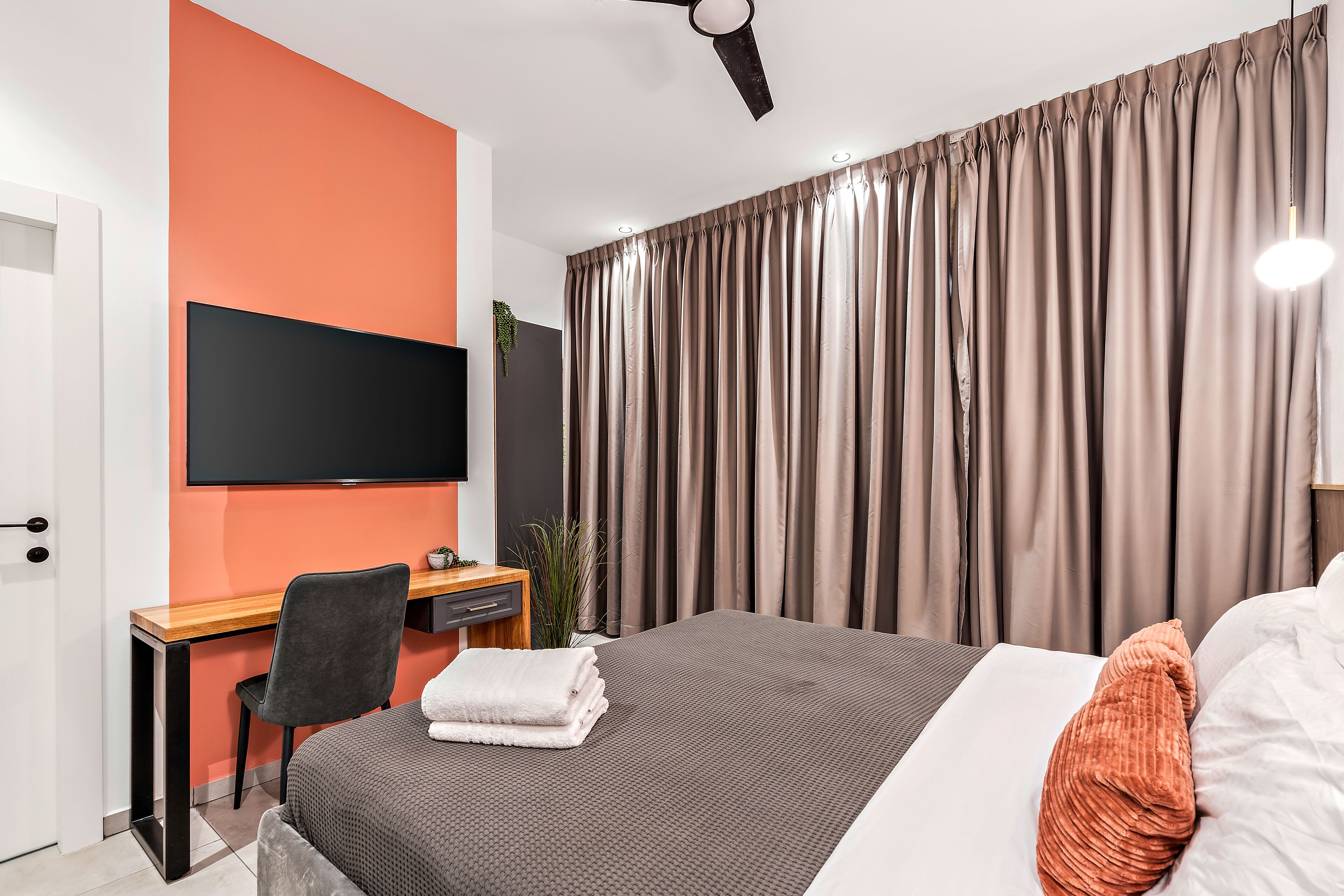A modern hotel room with a large bed, a desk, a flat-screen TV, and a window with curtains.