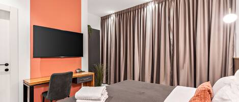 A modern hotel room with a large bed, a desk, a flat-screen TV, and a window with curtains.