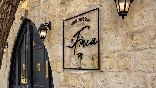 A stone wall with a sign for "Luxury Suites Hotel La Finca" and a black arched entrance with golden accents.
