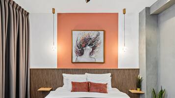 A modern hotel room with a large bed, a wooden headboard, a framed abstract painting, bedside tables with lamps, and potted plants.
