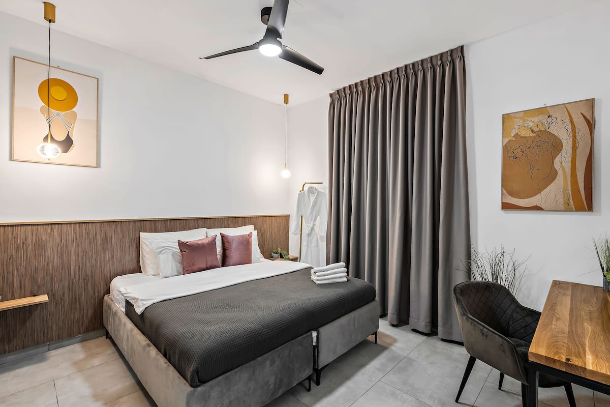 Ein modernes Hotelzimmer mit Bett, Schreibtisch, Stuhl, Deckenventilator und Kunstwerken an den Wänden.