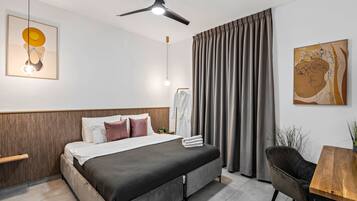 Una habitación de hotel moderna con una cama, un escritorio, una silla, ventilador de techo y obras de arte en las paredes.