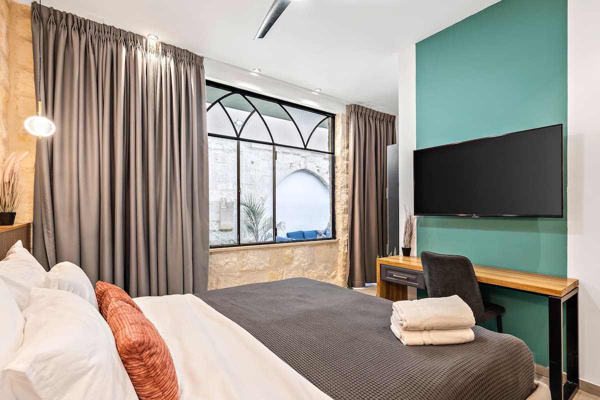 Ein Hotelzimmer mit Bett, Schreibtisch, Stuhl, Fernseher und einem Fenster mit Vorhängen.