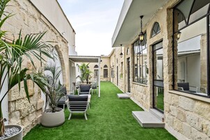 Un estrecho patio con césped verde, paredes de piedra y mobiliario exterior.