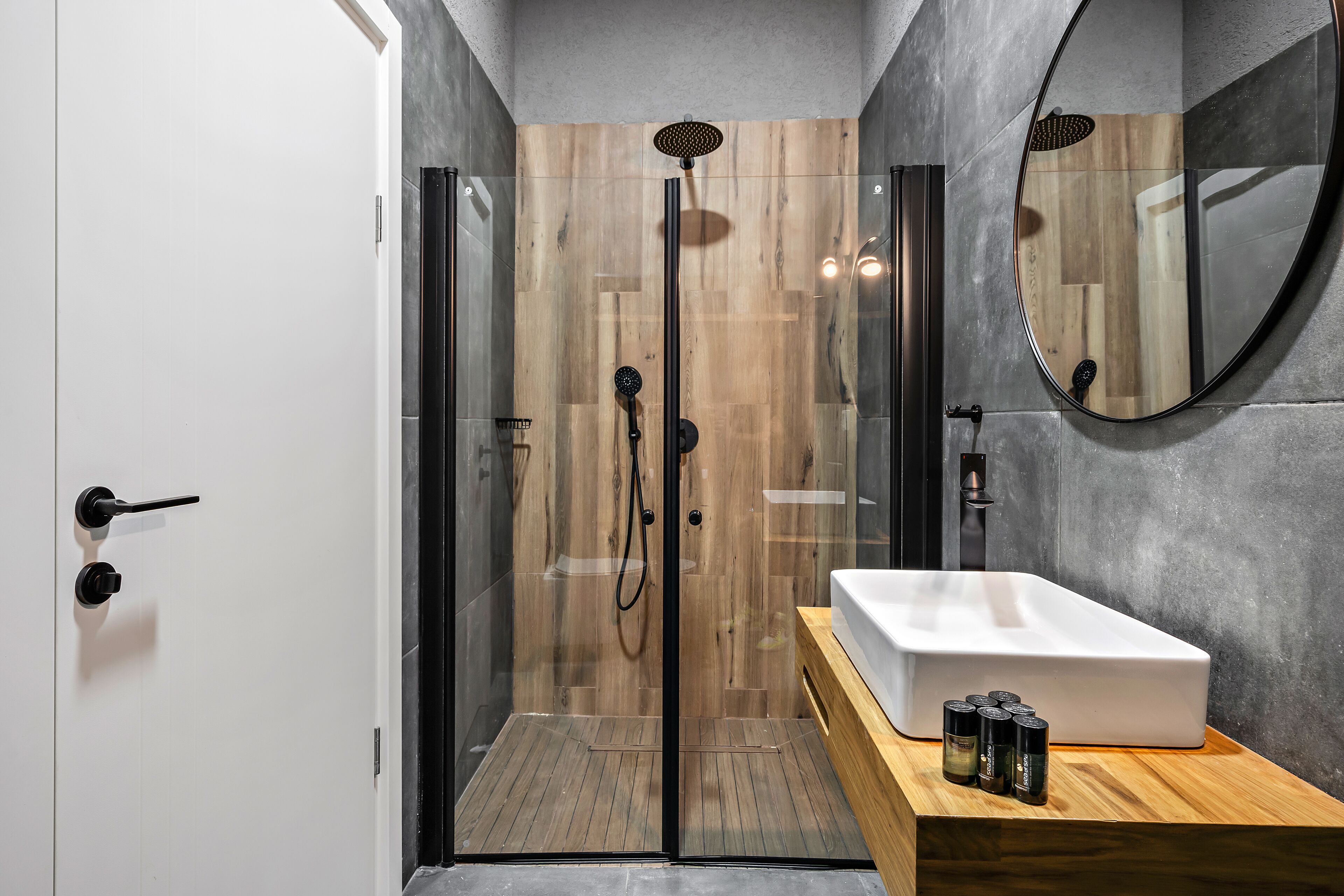 A modern bathroom with a glass-enclosed shower, a white sink, and a wooden vanity.