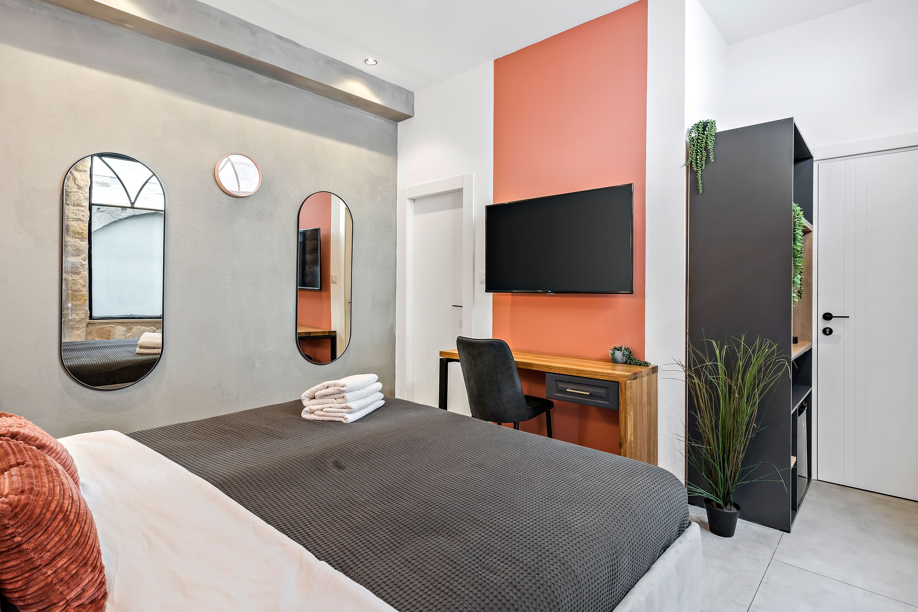 Una camera d'albergo moderna con un letto, una scrivania, una sedia, una TV e una pianta in vaso.
