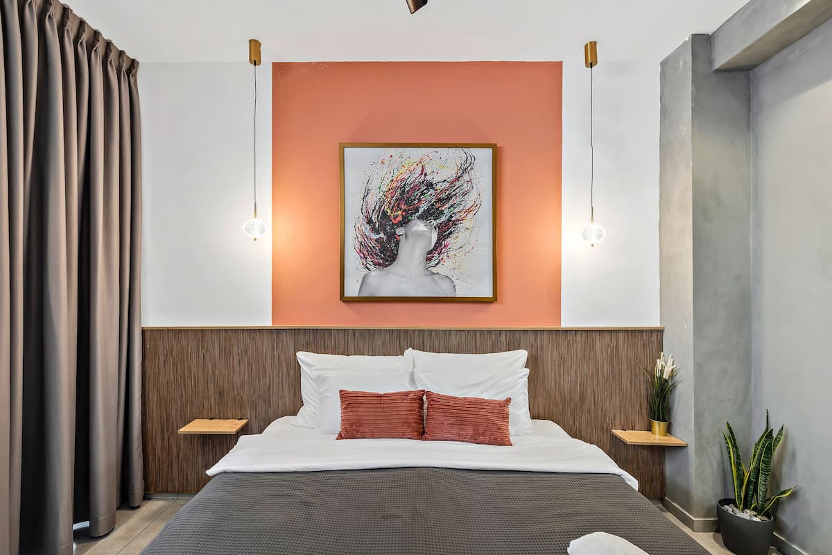 Ein modernes Hotelzimmer mit einem großen Bett, einem Holzwand-Kopfteil, einem gerahmten abstrakten Kunstwerk, Nachttischen mit Lampen und einer Topfpflanze.