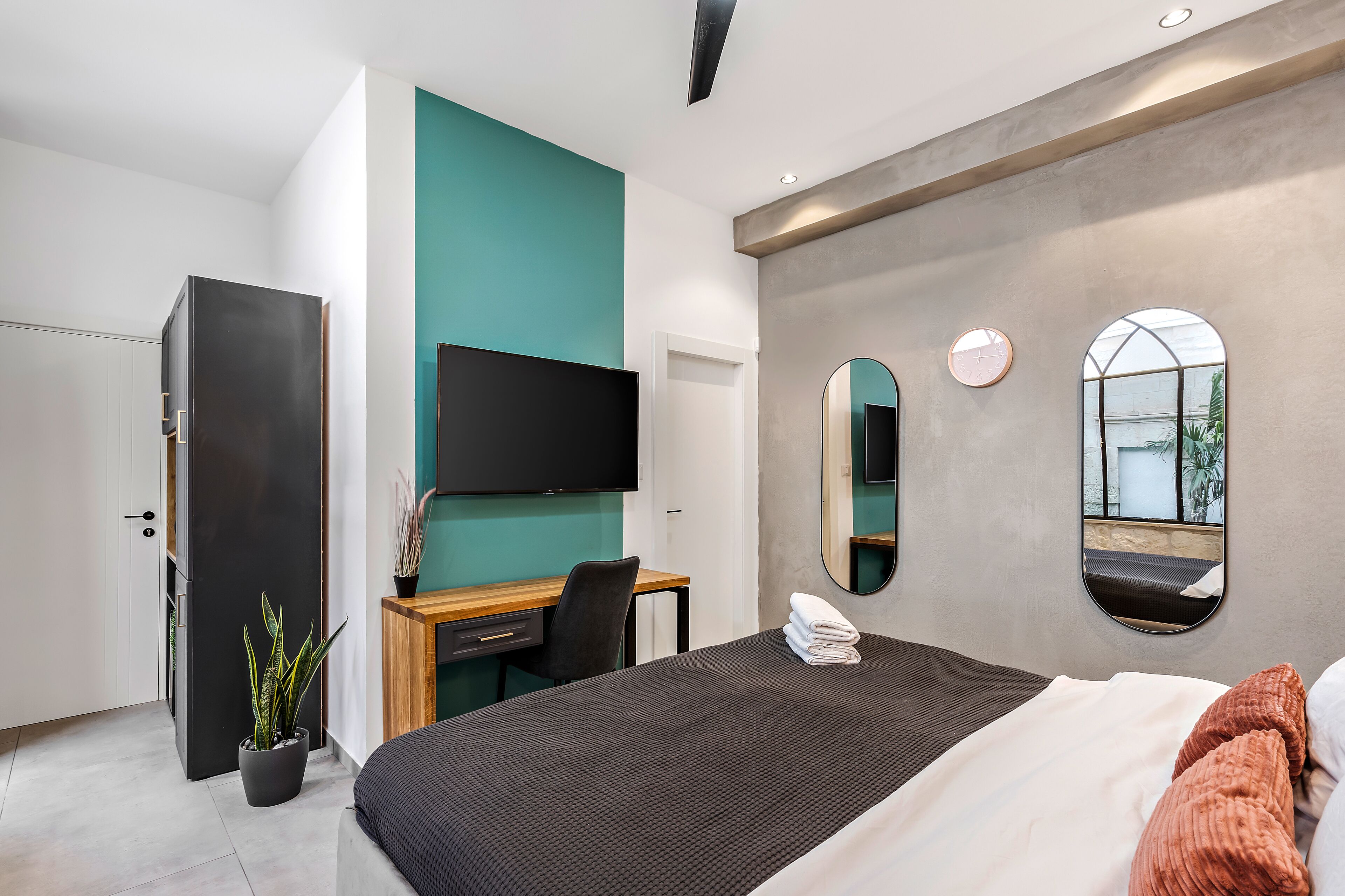 Habitación de hotel moderna con cama, escritorio, televisor y una planta en maceta.