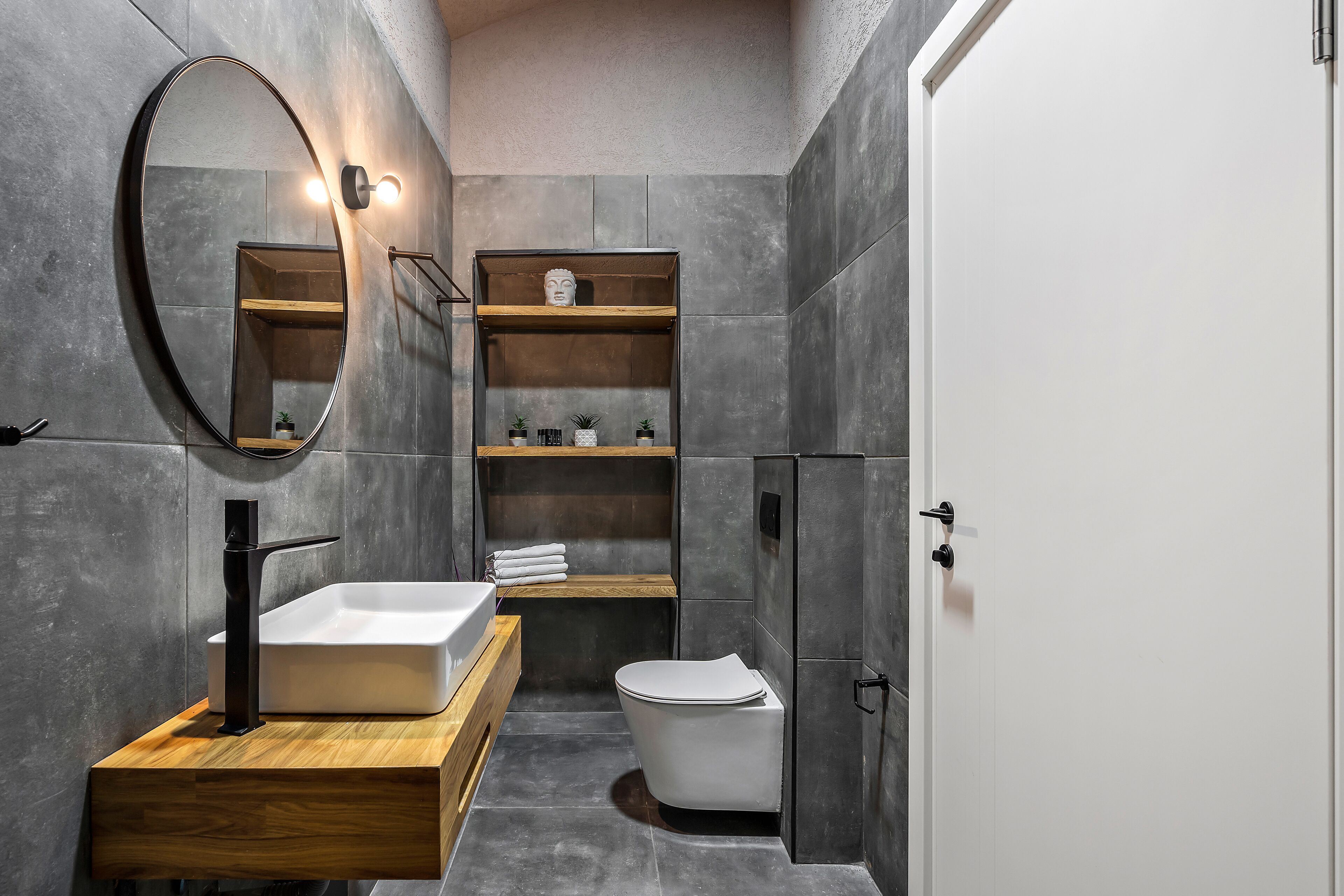 Un baño moderno con un lavabo rectangular, un inodoro y un mueble de tocador de madera. Hay un espejo sobre el lavabo y una repisa con objetos decorativos.