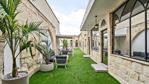 A courtyard with artificial grass, potted plants, outdoor seating, and stone walls.