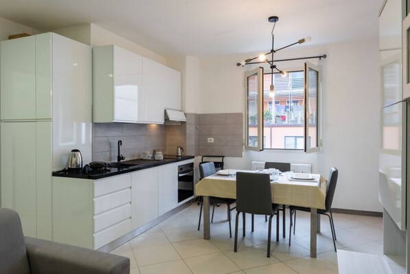 Une cuisine moderne avec des meubles blancs, une table à manger avec des chaises et une fenêtre avec des stores.