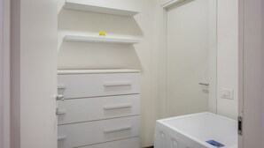 Una habitación pequeña y blanca con un armario blanco, una lavadora blanca y una puerta blanca.