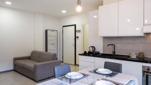 Una cocina moderna con armarios blancos, encimera negra y un comedor con una mesa para dos.
