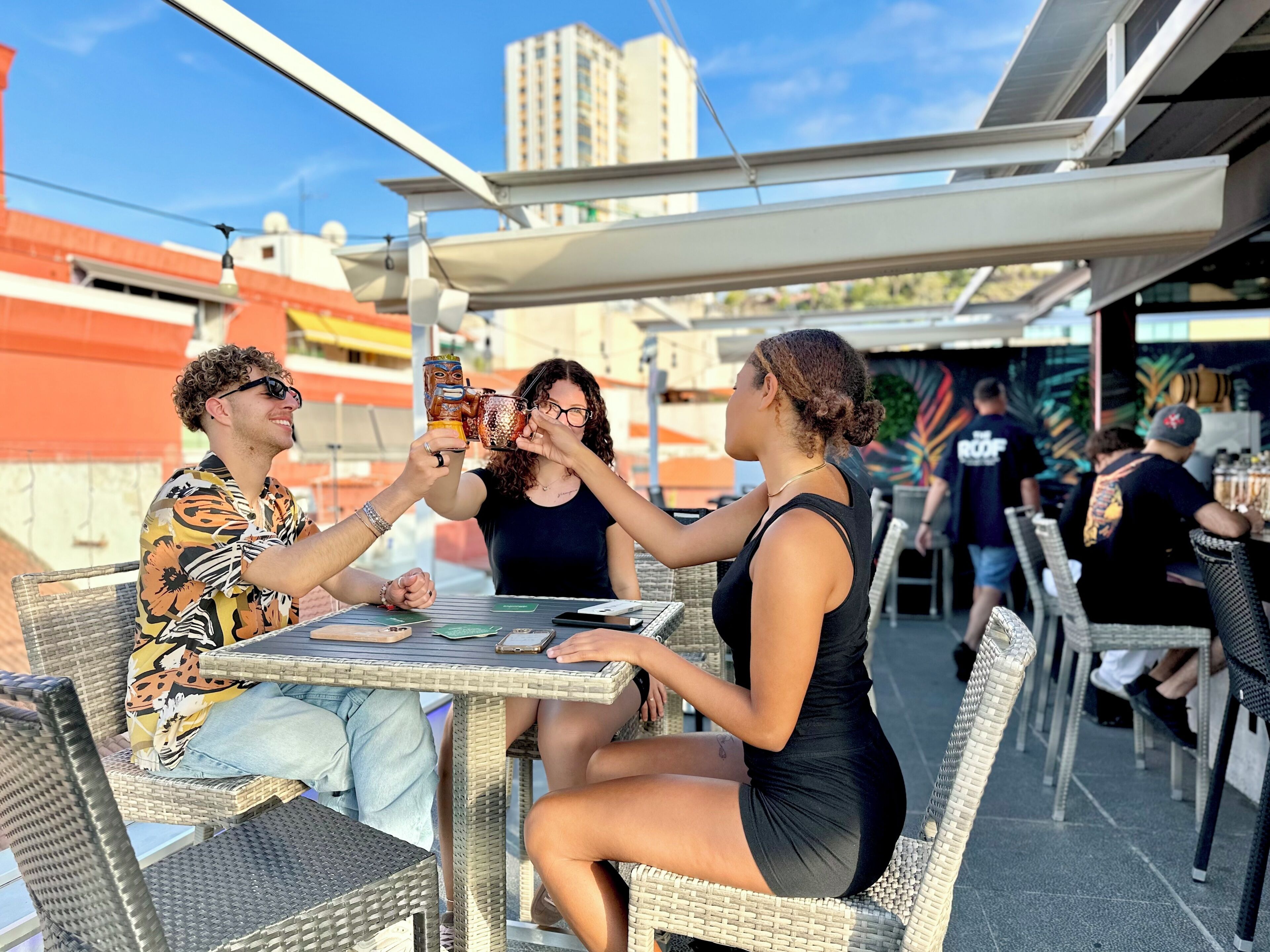 Un grupo de personas brindando en una mesa al aire libre con un paisaje urbano de fondo.