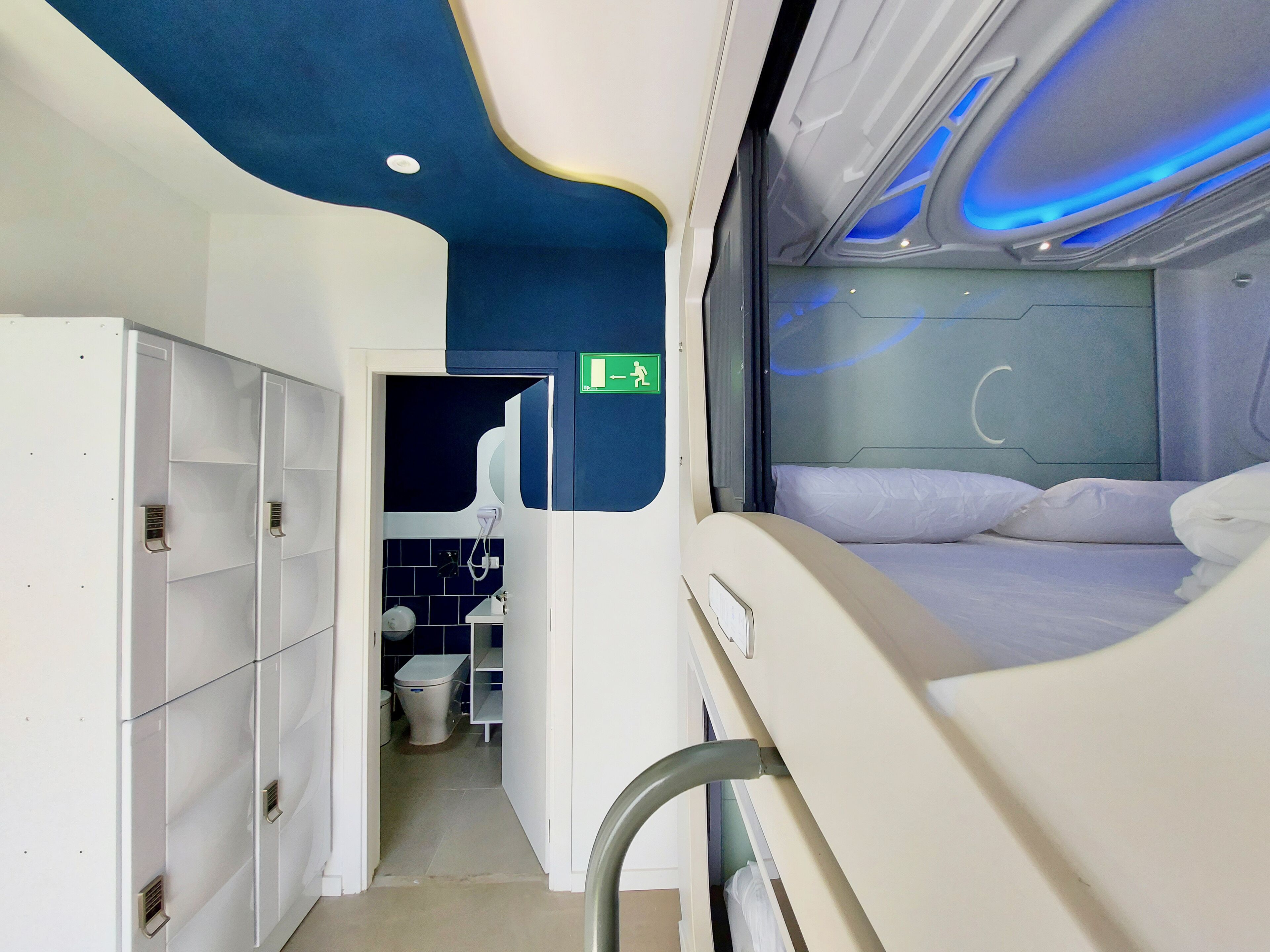 Een moderne treincoupé met een bed, bagagekastjes en een toilet.