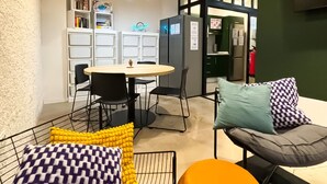 A modern interior with a round table, black chairs, a sofa with patterned cushions, and a kitchen area with a refrigerator and cabinets. - Atypicap Capsule Hostel (Puerto de la Cruz)